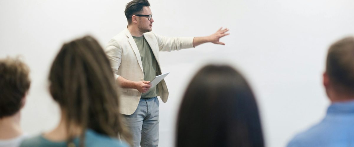 A man in a blazer gives a presentation to a captivated audience in a lecture setting.
